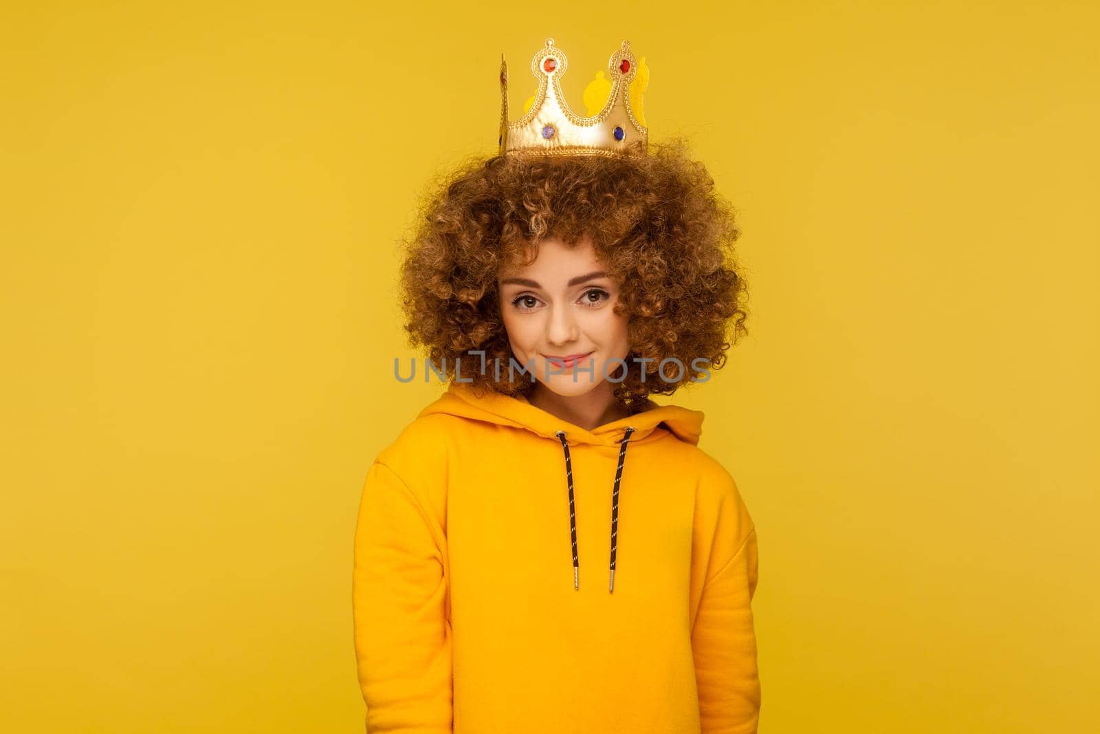 I am queen. Lovely happy curly-haired hipster woman wearing crown on head and smiling, concept of self confidence in success, self-motivation and dreams to be best. indoor studio shot, isolated