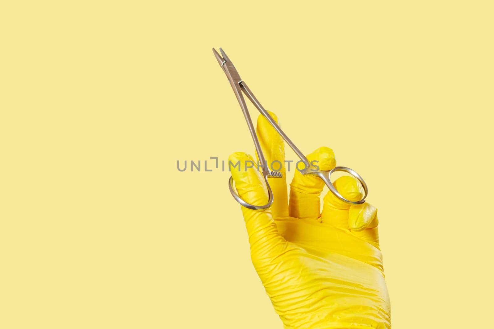 Woman's hand in a latex glove with stainless steel needle holder on yellow.