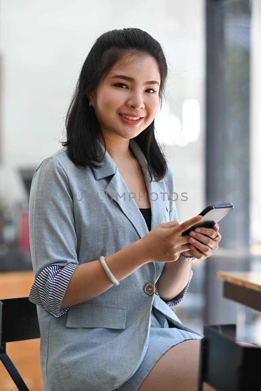 Portrait of beautiful young asian woman sitting in modern coffee shop and using mobile phone. by prathanchorruangsak