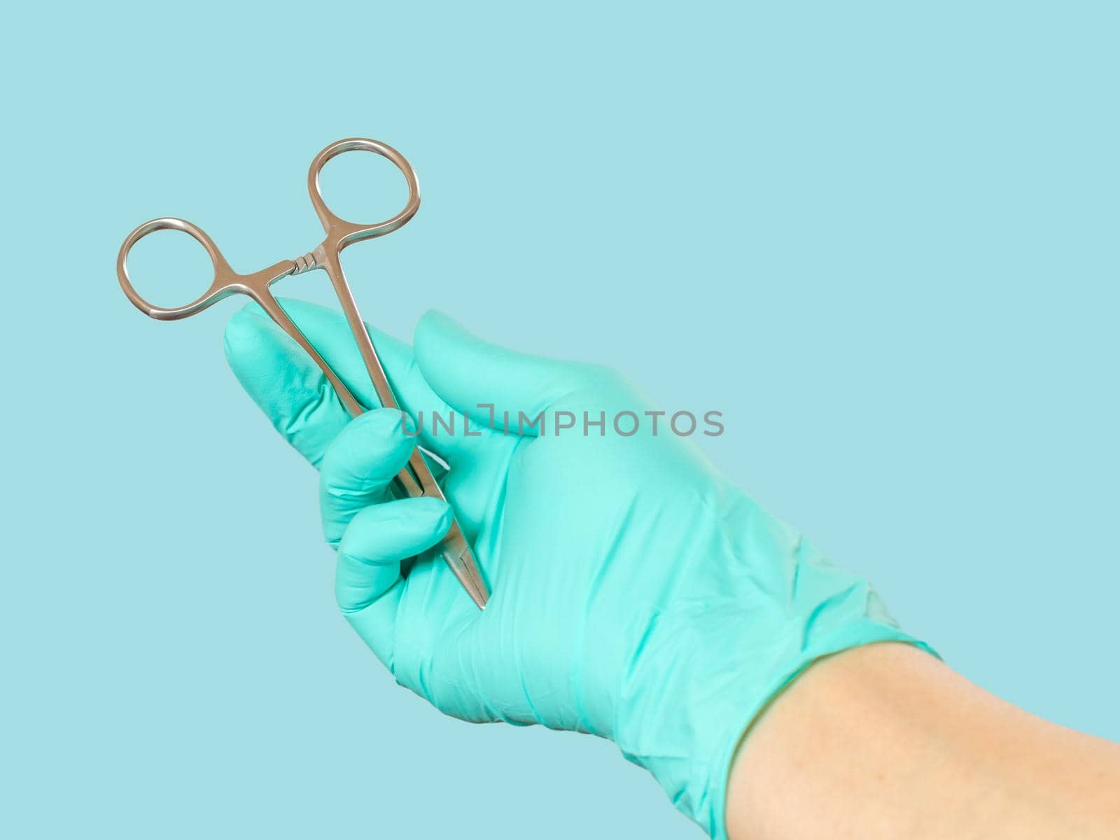 Woman's hand in a latex glove with stainless steel needle holder on green mint.