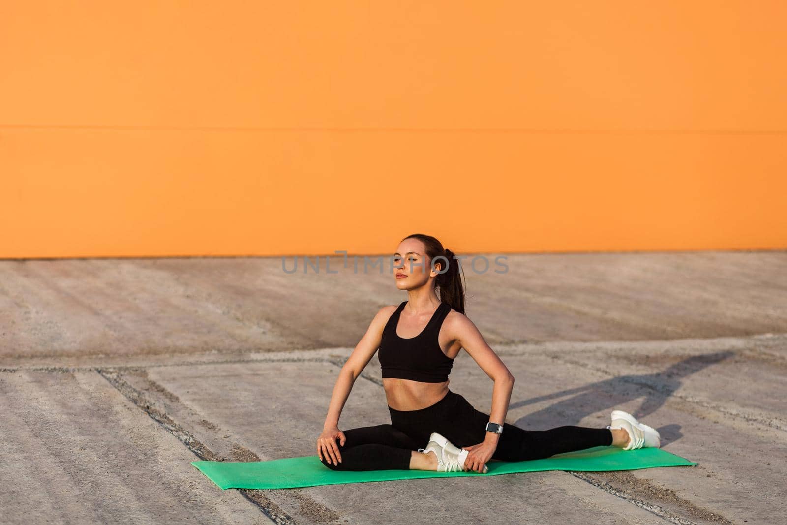 Motivated athletic positive woman in tight sportswear, black pants and top, practicing yoga, doing one legged king pigeon pose and meditating, flexibility training. Health care, sport activity outdoor