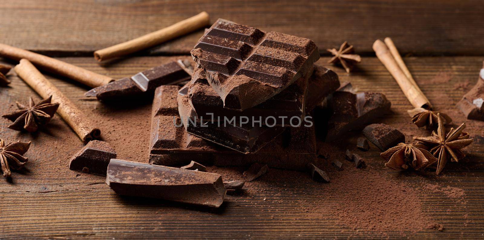 broken pieces of dark chocolate, cinnamon sticks and star anise on a brown wooden table, top view