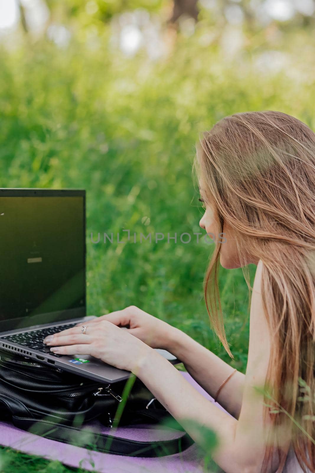 On the banner, a young girl works with a laptop in the fresh air in the park, sitting on the lawn. The concept of remote work. Work as a freelancer. The girl takes courses on a laptop and smiles