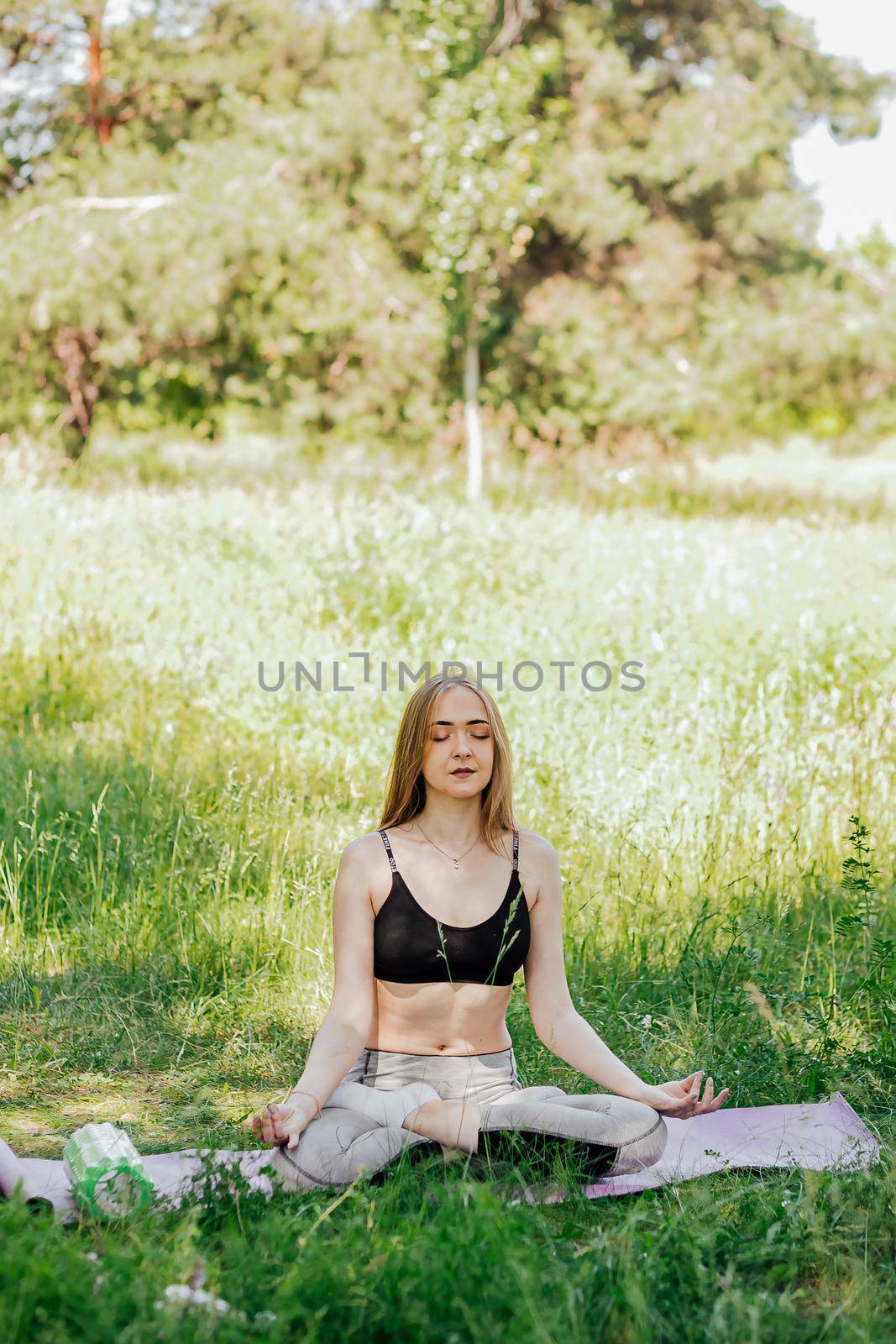 Yoga woman on green grass girl relaxes in the field. Yoga woman in green park girl doing gymnastics outdoors. Meditating woman in meditation in yoga pose practices outdoors