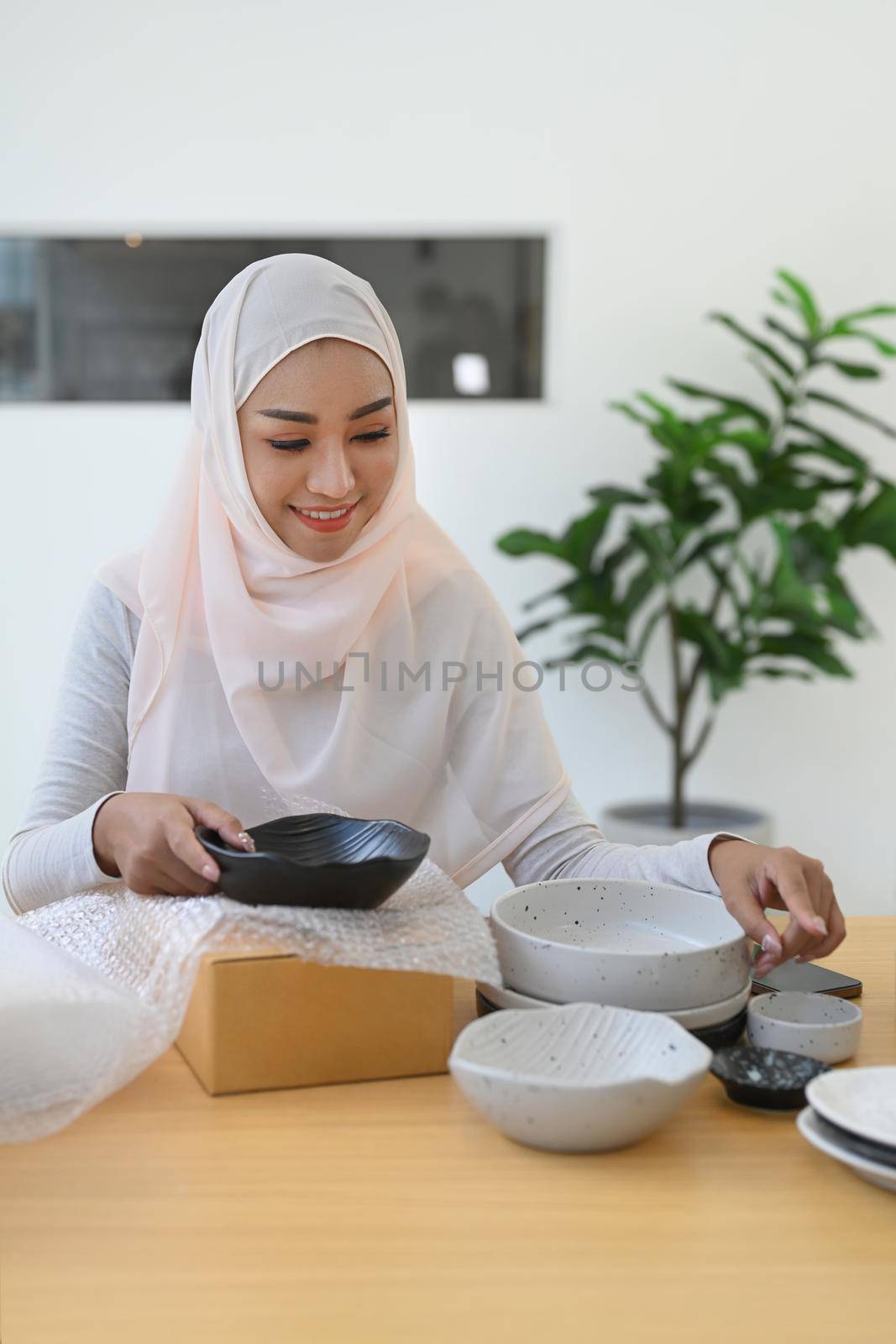 Beautiful Muslim woman online seller packing product in cardboard box for shipping to customers by prathanchorruangsak