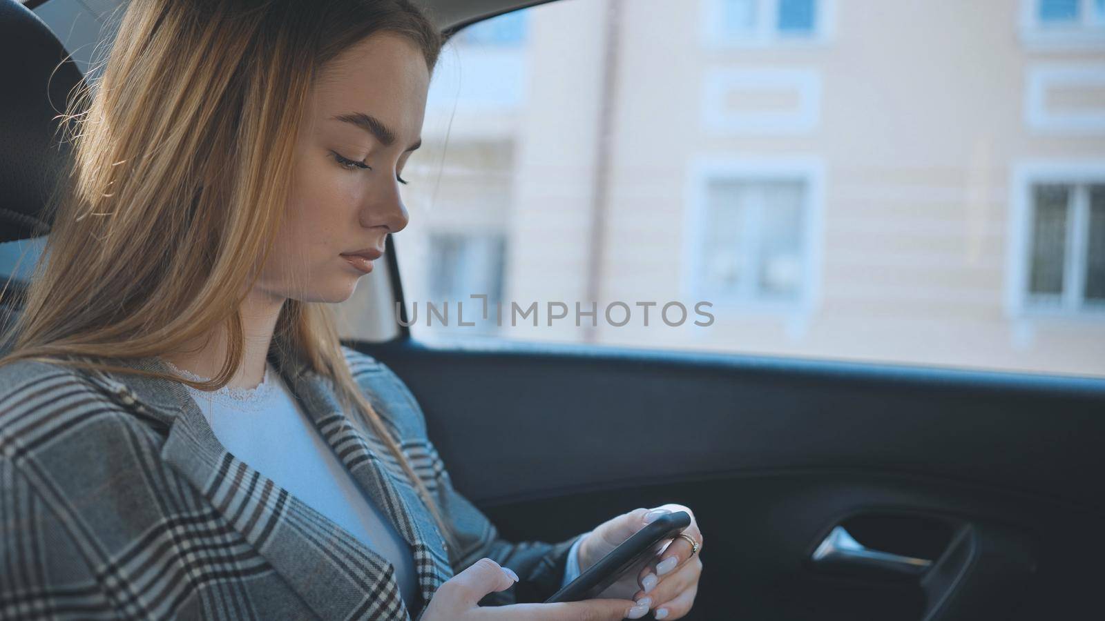 A young girl rides in the backseat of a car and watches her smartphone