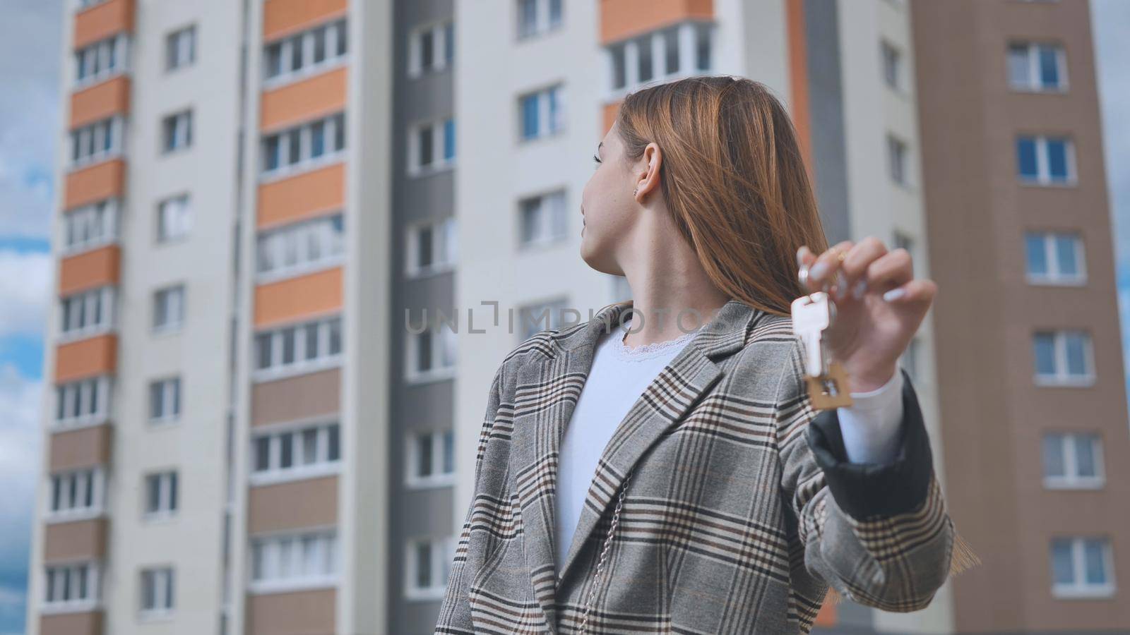 The girl shows the keys to the apartment against the backdrop of an apartment building