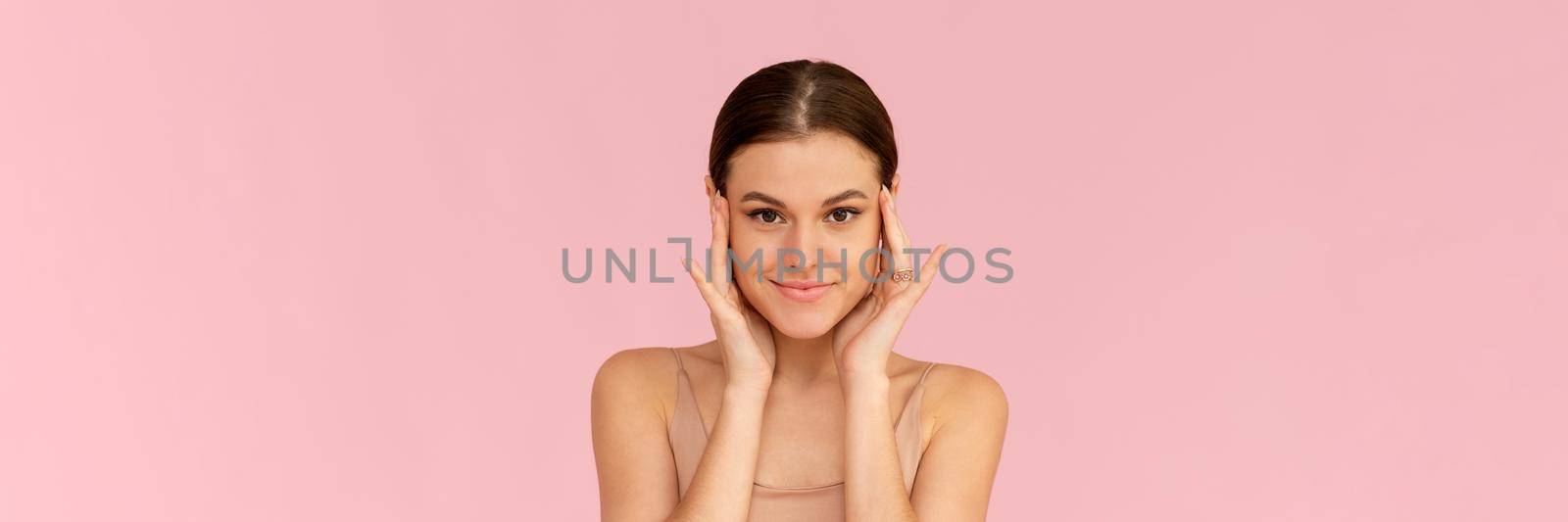 Skin care. Woman with beauty face touching healthy facial skin. Smiling female model looking at the camera and smiling over pink background. Web banner.