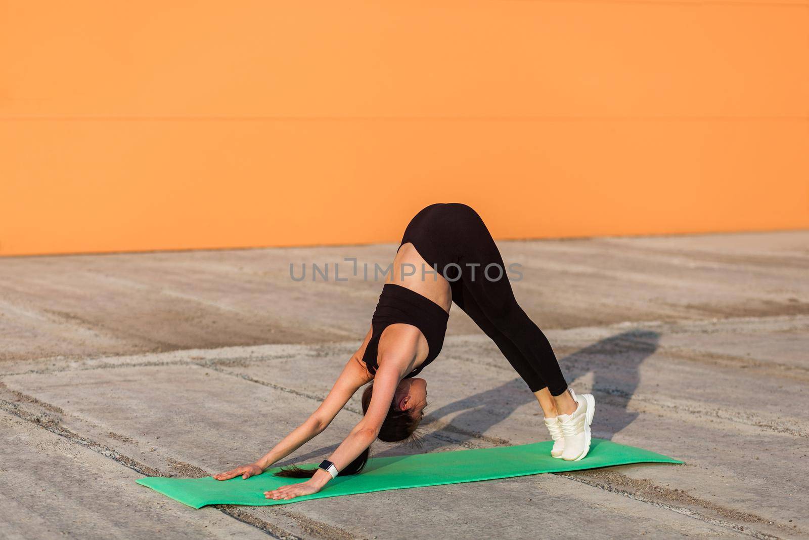 Slim athletic woman in tight sportswear, black pants and top, practicing yoga, standing downward facing dog pose, stretching body muscles, flexibility training. Health care, sport activity outdoor