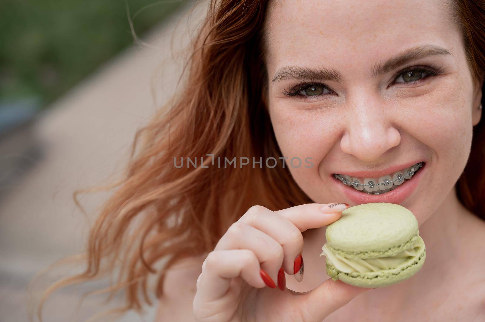 Young red-haired woman with braces eating macaron cake. by mrwed54