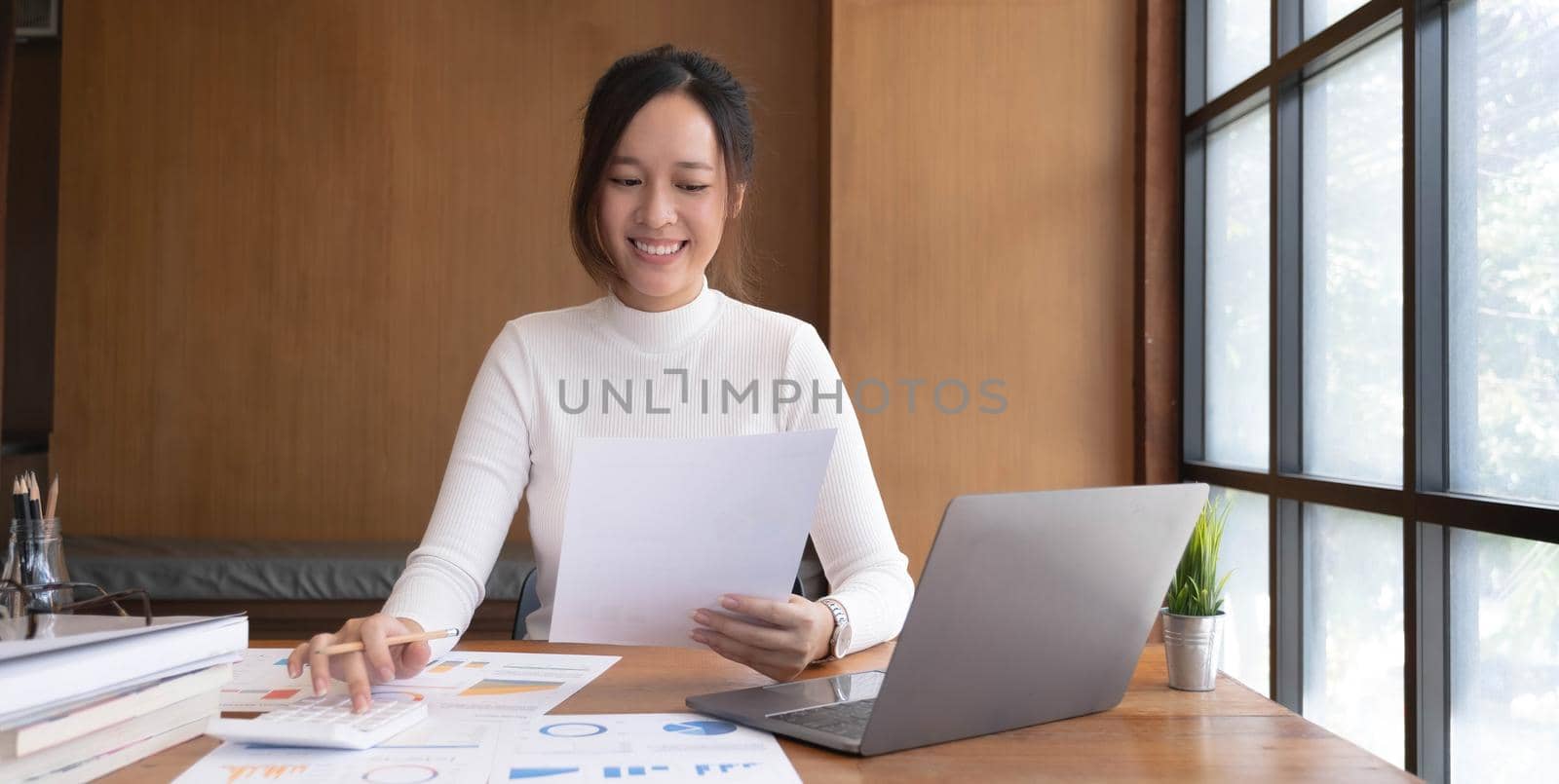 Portrait of Young Asian woman hand freelancer is working her job on computer tablet in modern office. Doing accounting analysis report real estate investment data, Financial and tax systems concept. by wichayada