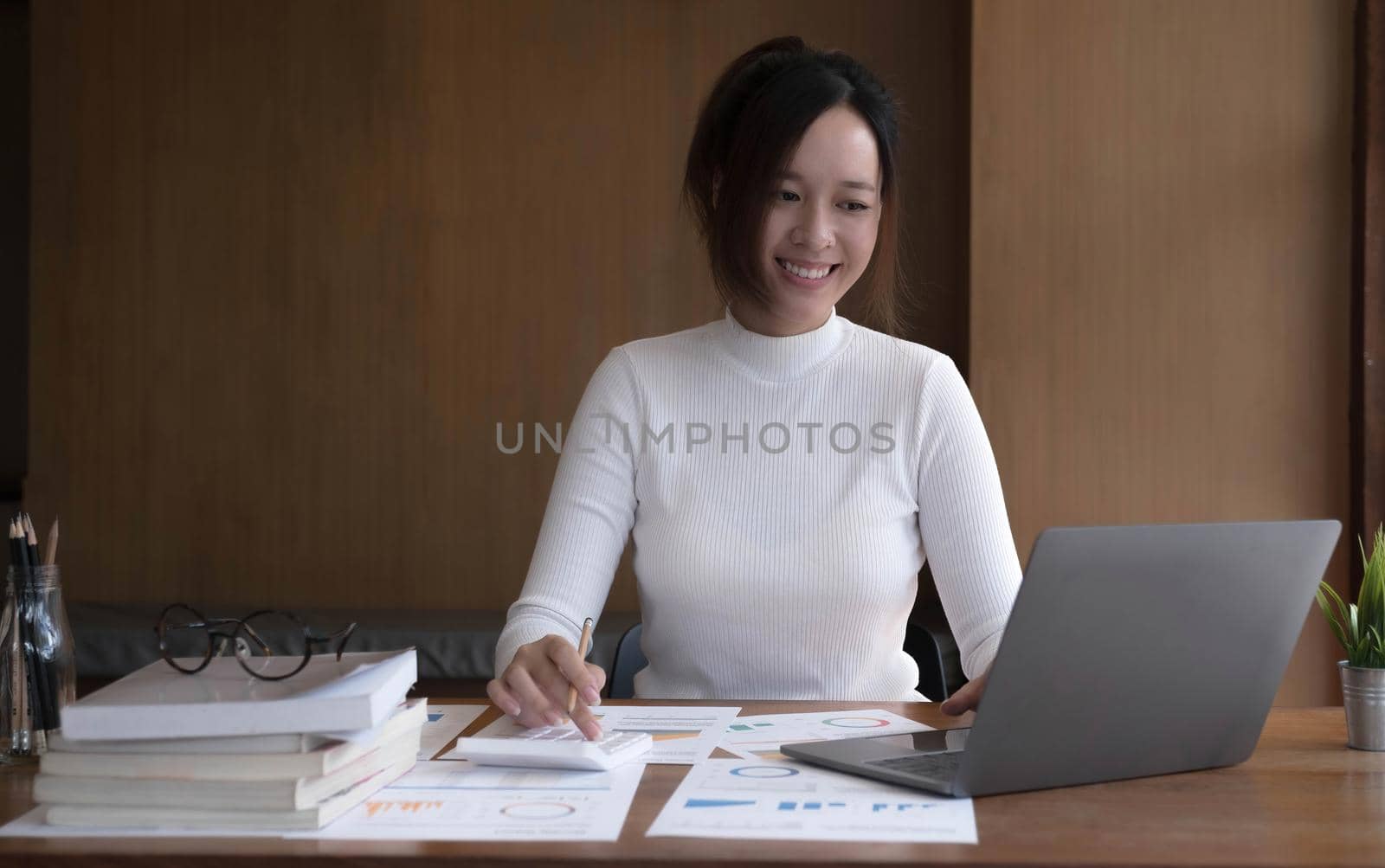Attractive young Asian businesswoman or office worker working at her desk, using laptop computer to analyse her financial data. by wichayada