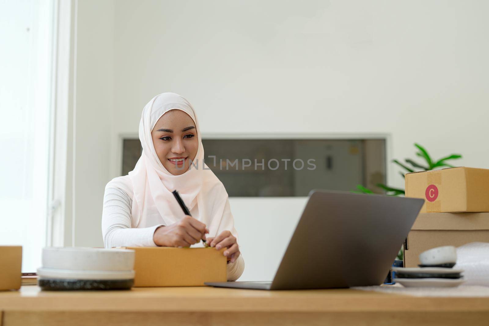 Happy young muslim woman owner writing address on cardboard box, Young Owner Woman Start up for Business Online. People with online shopping SME entrepreneur or freelance working concept