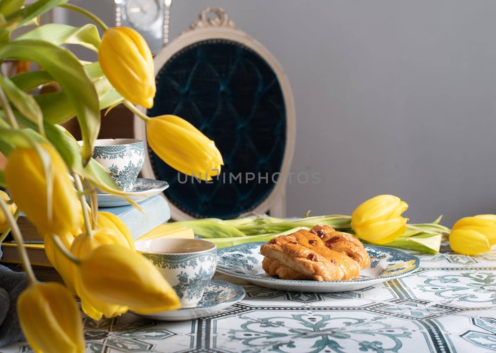 retro still life, sweet puff, tea in a vintage porcelain cup and a stack of books, a bouquet of yellow withering tulips in a vase,. High quality photo