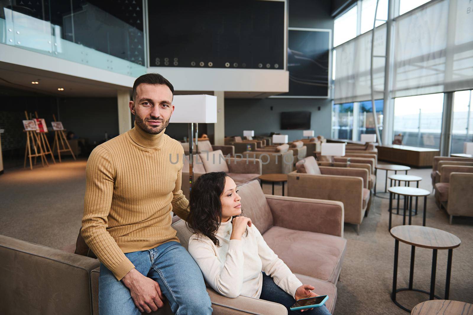 Business partners, handsome friends waiting for a flight in the VIP lounge of the departure area of international airport. Charming Middle-Eastern young married couple traveling in their honeymoon.