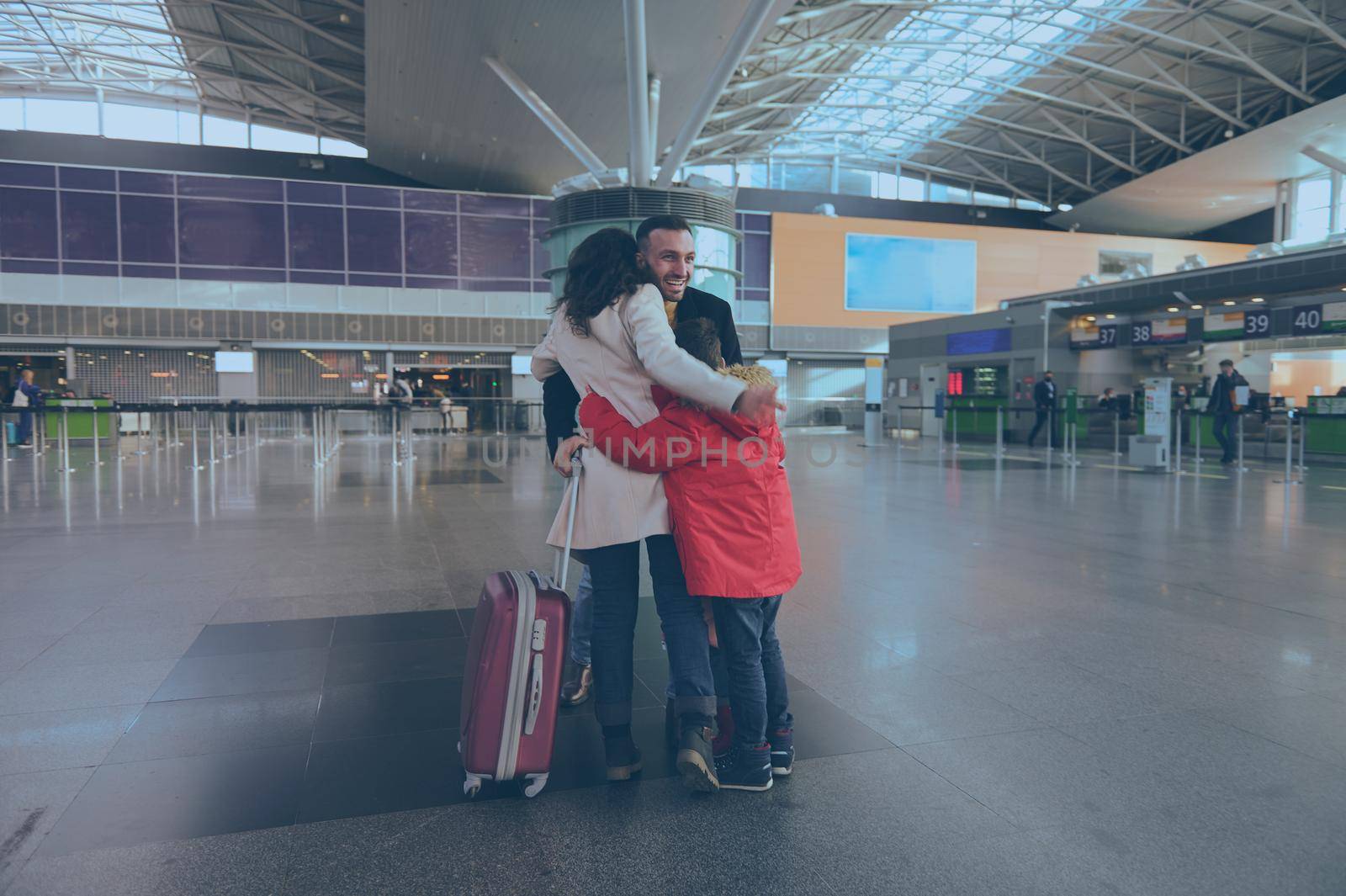 Happy young Caucasian man, his wife and children greeting each other after long separation at airport building. Long-awaited family reuniting by artgf