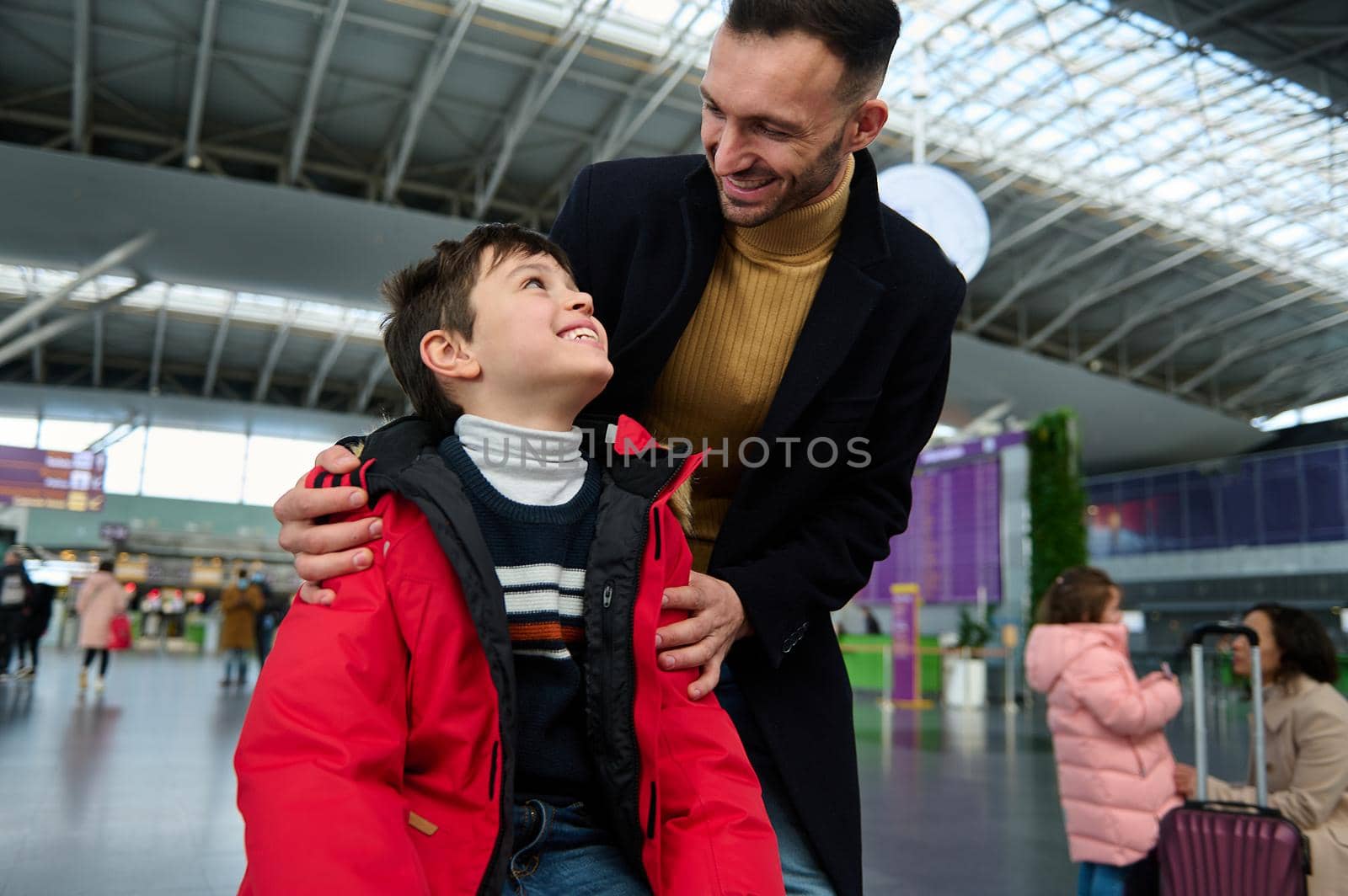 Happy young father with his adorable son in the departure hall of an international airport, waiting for flight check-in, customs control and boarding. Travel by air, winter tourism, vacation concept