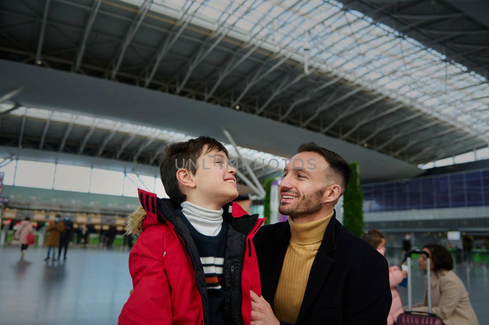 Happy young father communicates with his cute son while waiting for customs control in the departure terminal of an International airport. Family traveling, vacations, air travel and tourism concept