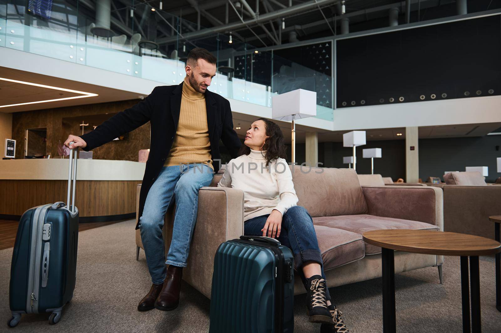 Charming young couple in love, married heterosexual couple, business partners, travelers, passengers with suitcase relaxing in the VIP lounge, waiting for flight check-in at international airport