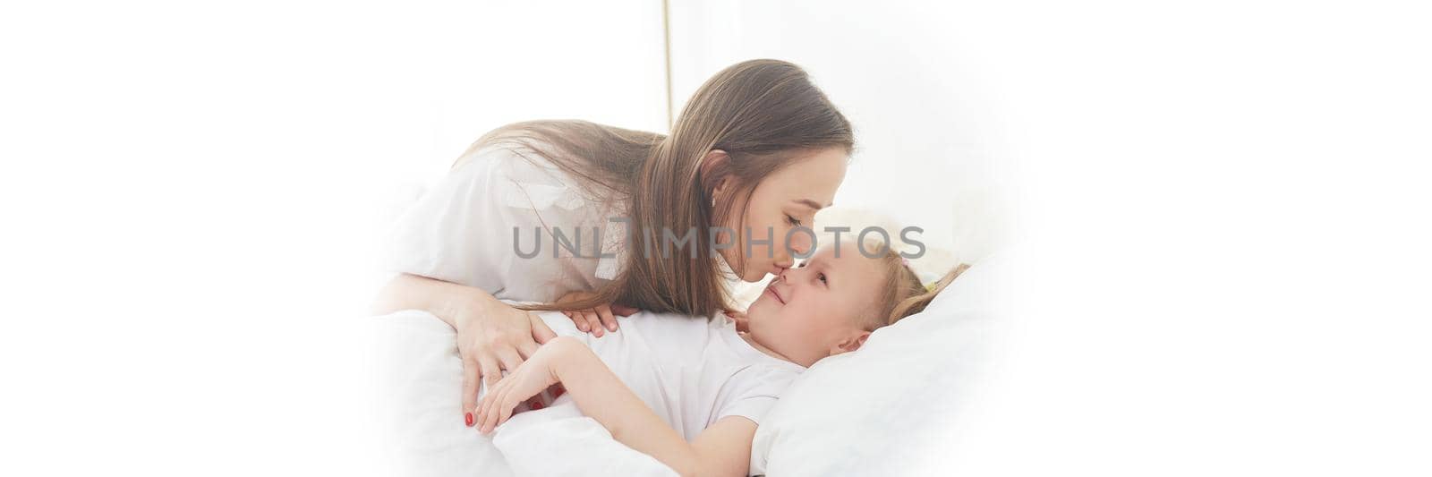 Awakening to a happy day. Mom wakes up her little daughter with a kiss on the bed in the bedroom. Web banner by etonastenka