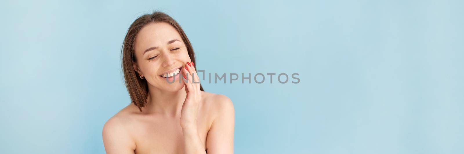 Smiling woman touching her face against a blue background. Natural beauty concept, happy woman. Web banner