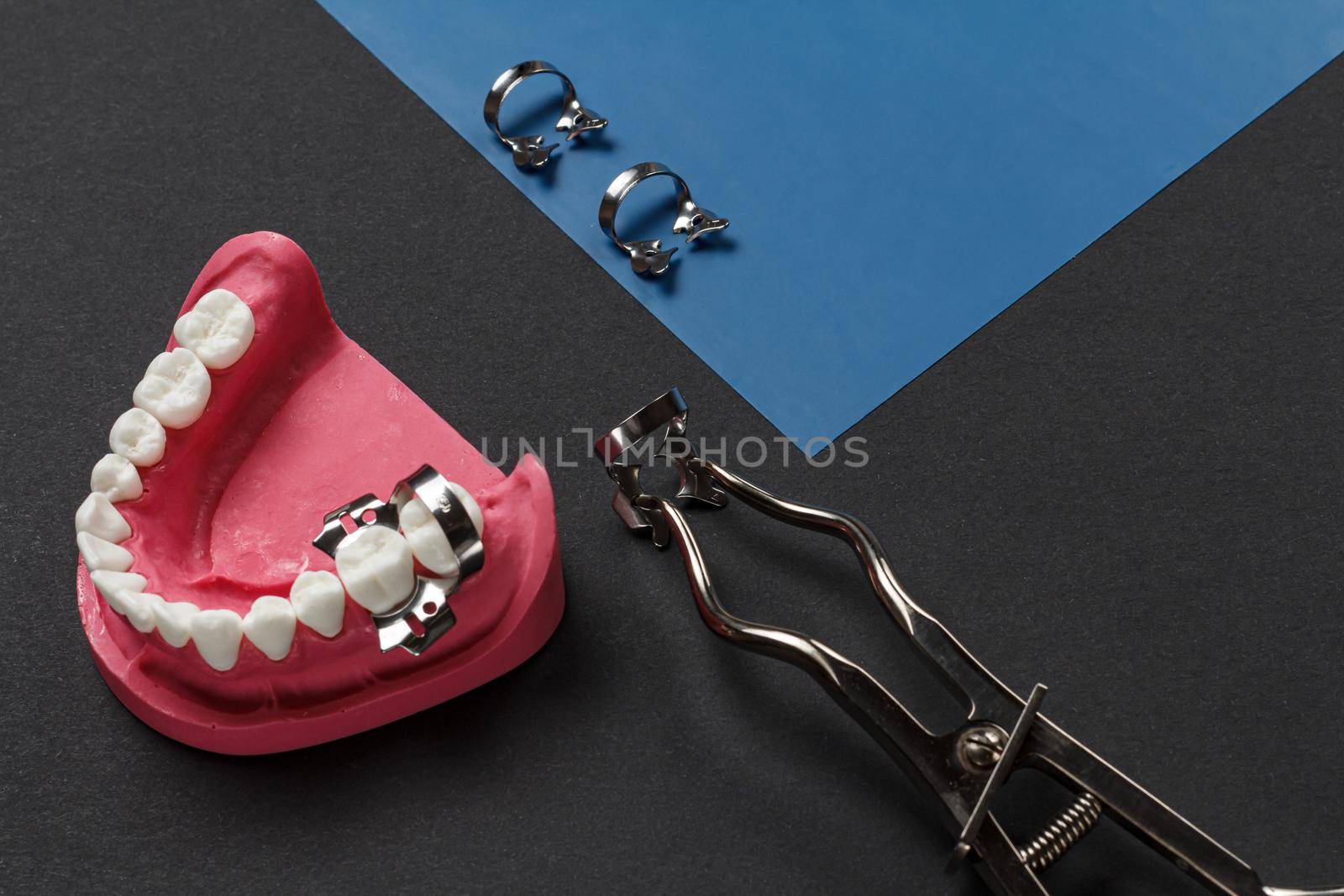 Layout of the human jaw, a rubber dam with dental dam clamps and a rubber dam clamp pliers on the black background. Medical tools concept. Top view.