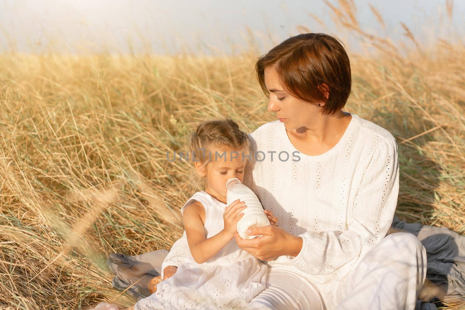 Little girl with her mother drink milk plastic bottle. Happy family, daughter with mom resting outdoor drink healthy diary product by andreonegin