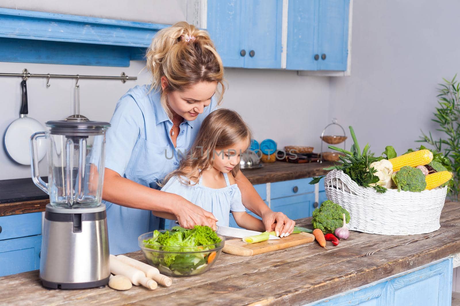 Young mother and lovely child cooking healthy breakfast together, cutting chopping vegetables, preparing vegetarian salad in modern kitchen, fresh green vegetables on table, vegan food, diet nutrition