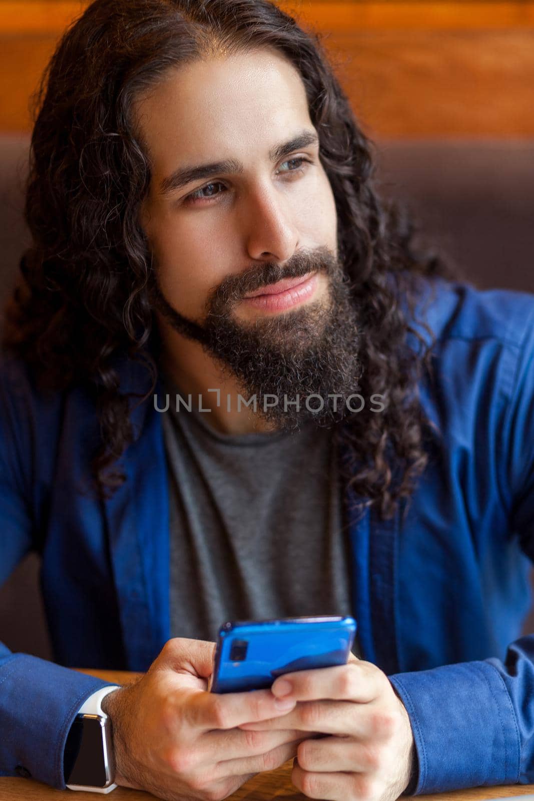 Close up portrait of cheerful handsome intelligence young adult man freelancer in casual style sitting in cafe, holding phone and looking away, bussinessman in office. Indoor, lifestyle concept