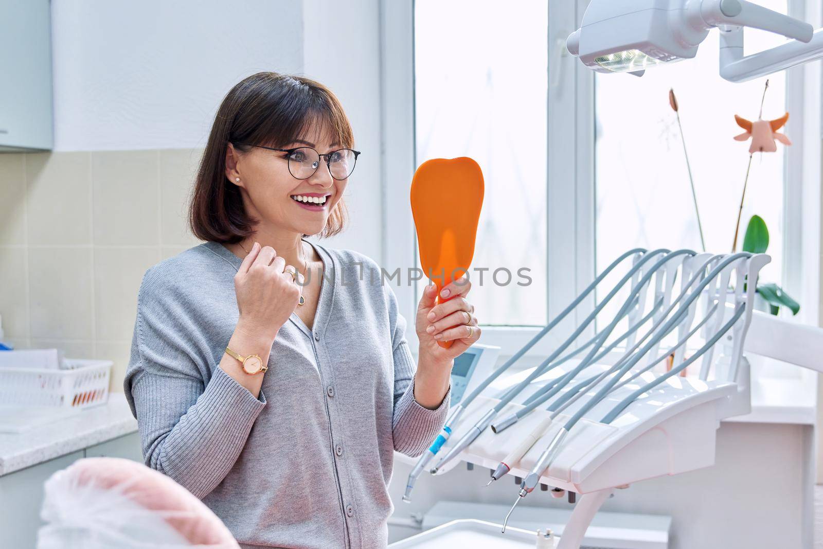 Happy woman dentist patient with mirror in hands looking at her teeth by VH-studio