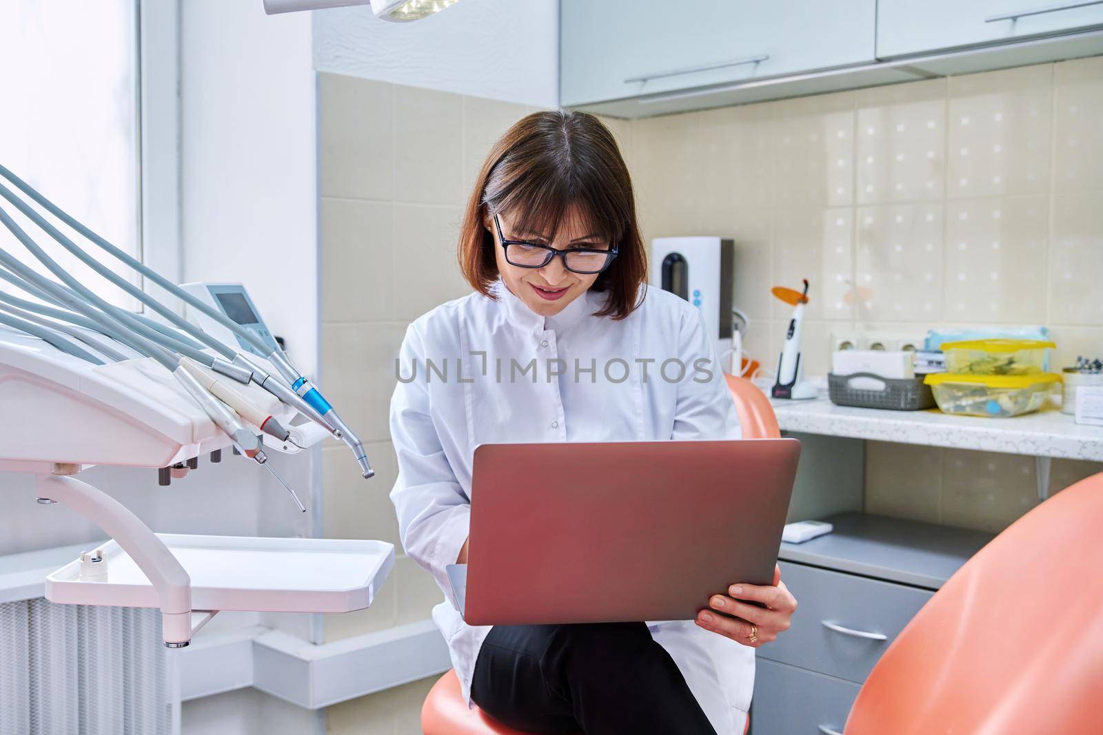 Doctor dentist sitting in the office using a laptop. Dentistry, health care, treatment, work, profession, medicine concept