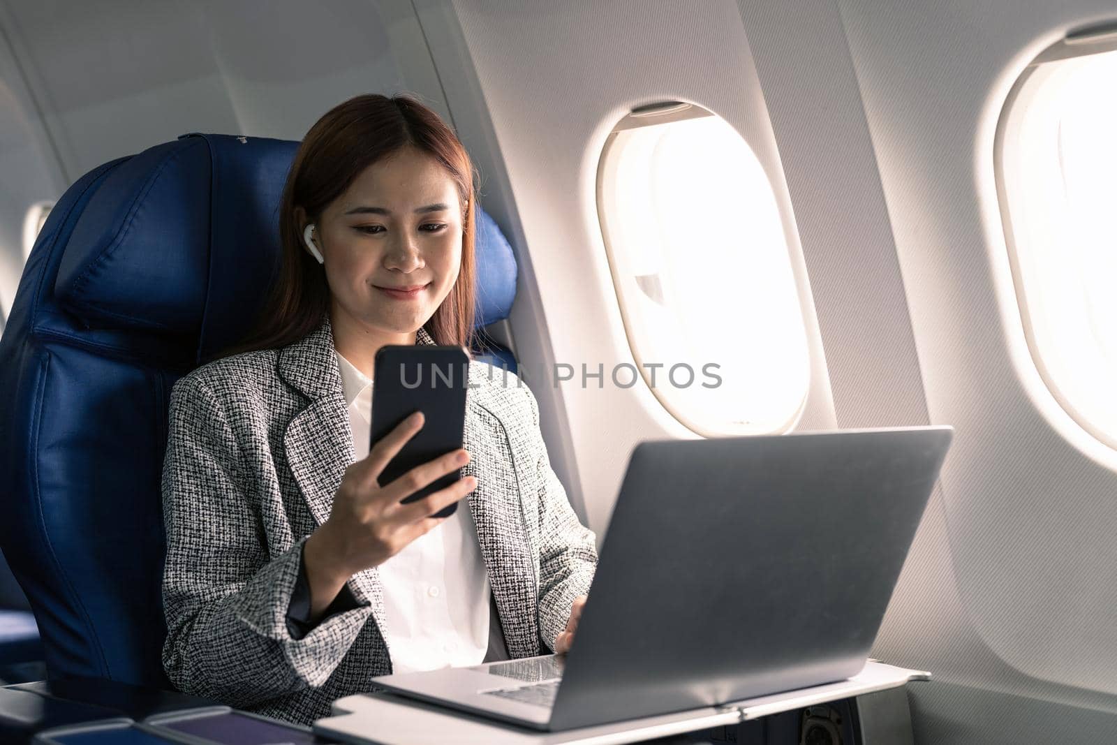 Happy and cheerful asian businesswoman using smartphone and laptop computer during flight. Urban lifestyle.