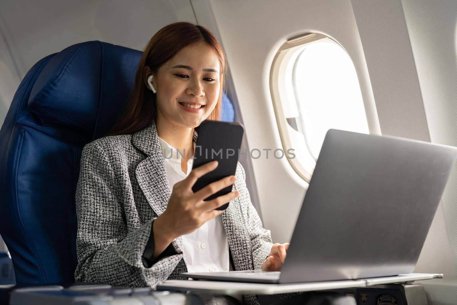 Happy and cheerful asian businesswoman using smartphone and laptop computer during flight. Urban lifestyle.