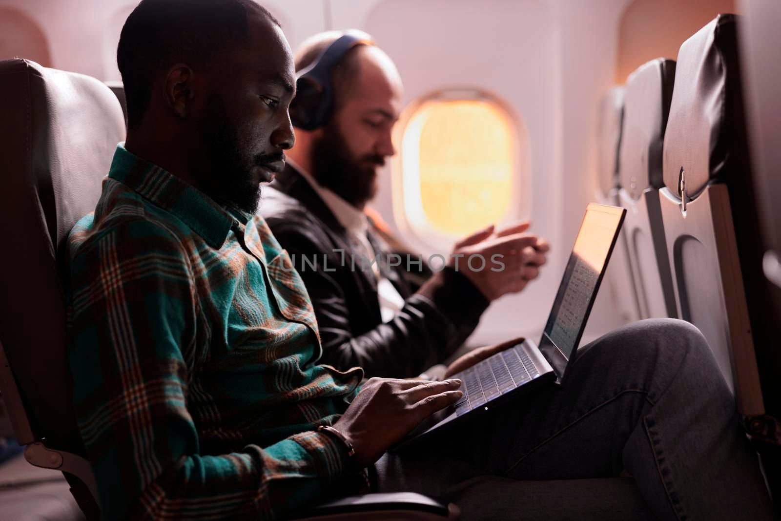 African american passenger working on laptop during sunset flight by DCStudio