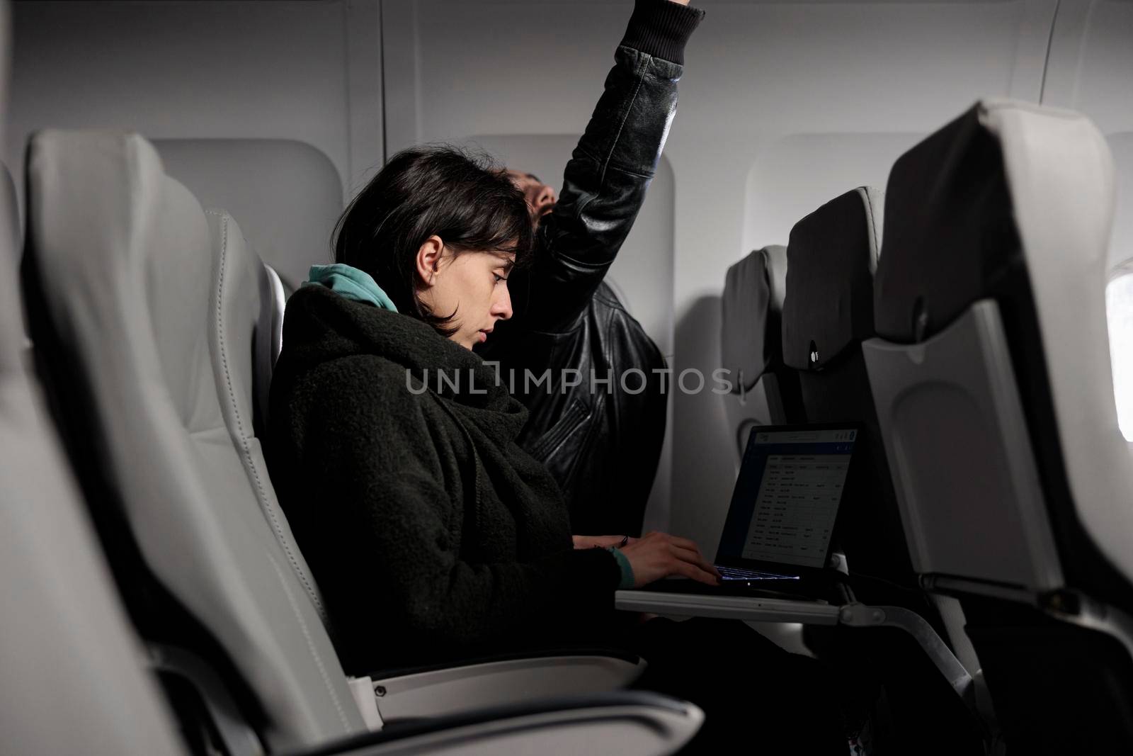Young adult working on laptop during airplane flight abroad, using online internet on computer to travel to holiday destination. Tourist waiting to arrive after commercial flight transportation trip.