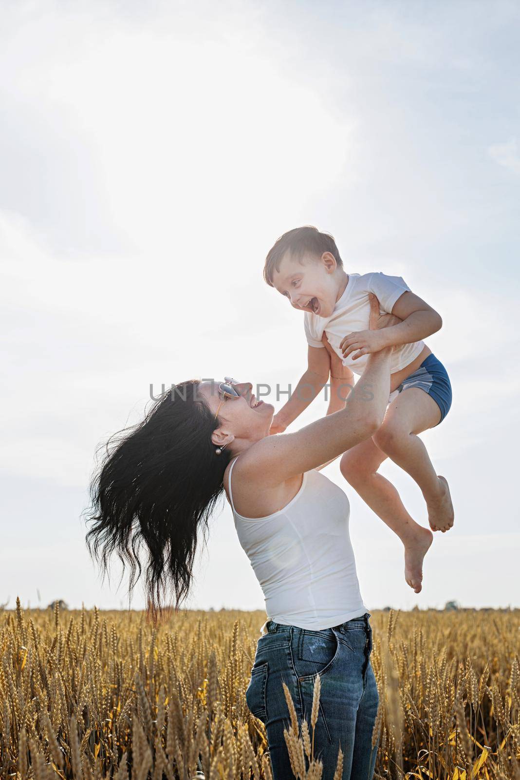 Happy family on a summer walk, mother and child walk in the wheat field and enjoy the beautiful nature, mom pick up child