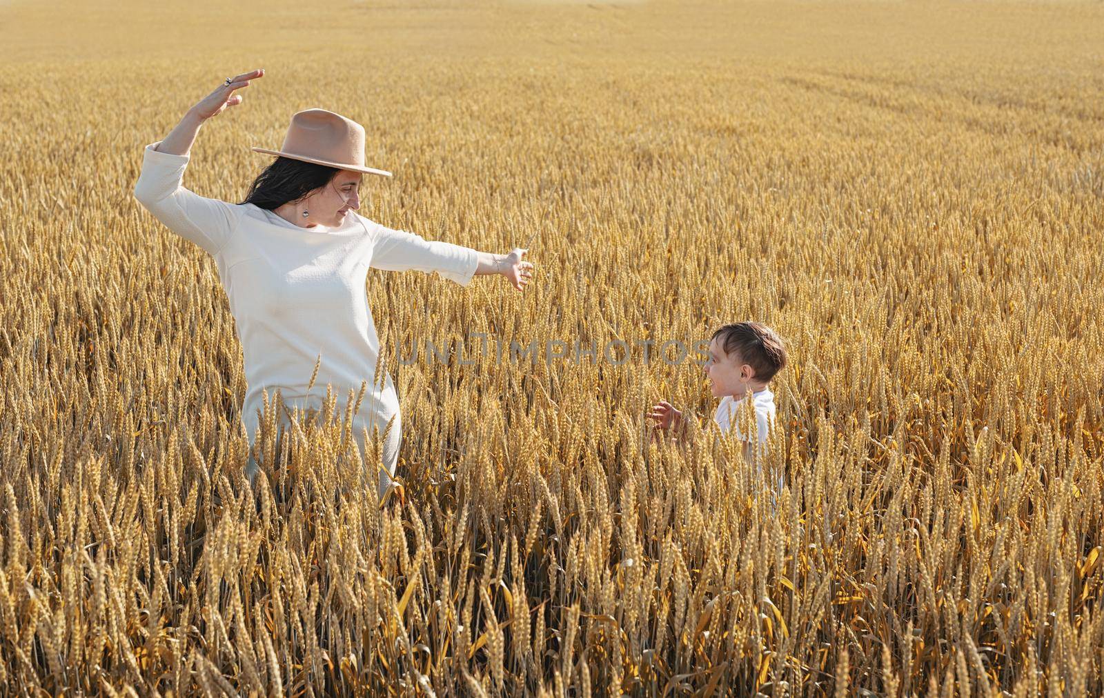 Happy family on a summer walk, mother and child walk in the wheat field and enjoy the beautiful nature, at sunset