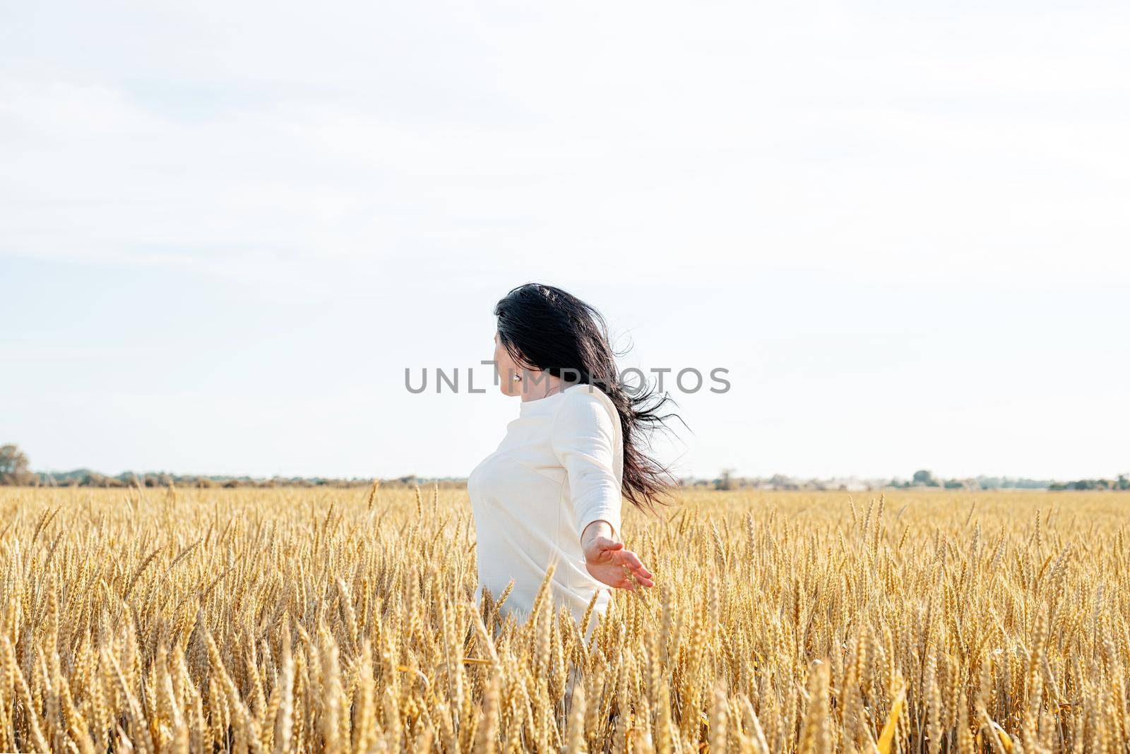 Mid adult woman in white dress standing on a wheat field with sunrise on the background, back view by Desperada