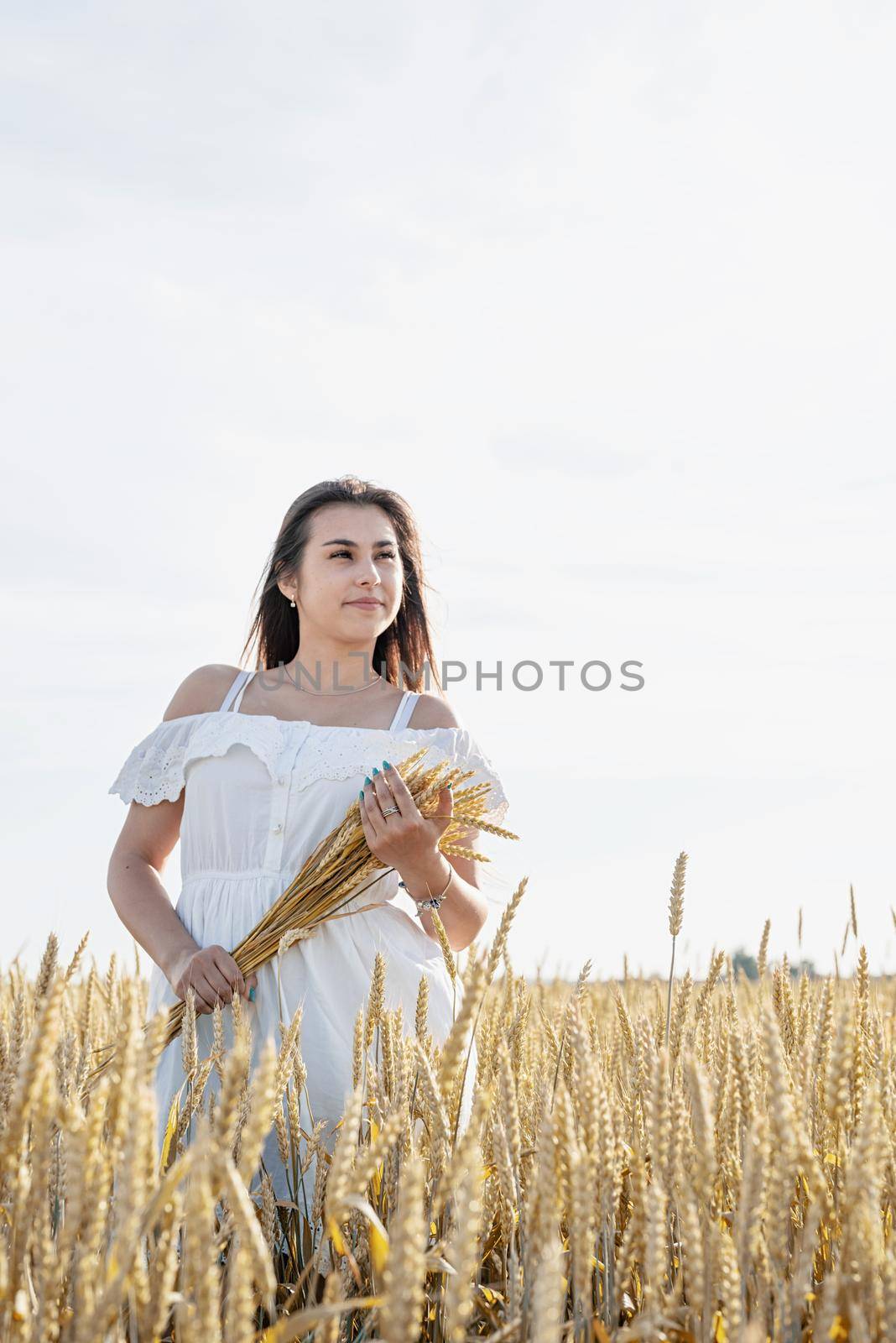 Young woman in white dress standing on a wheat field with sunrise on the background by Desperada