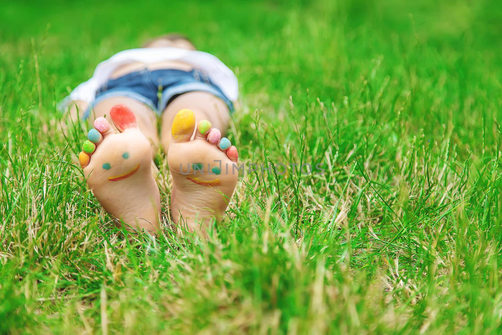 Children's feet with a pattern of paints smile on the green grass. Selective focus. by yanadjana