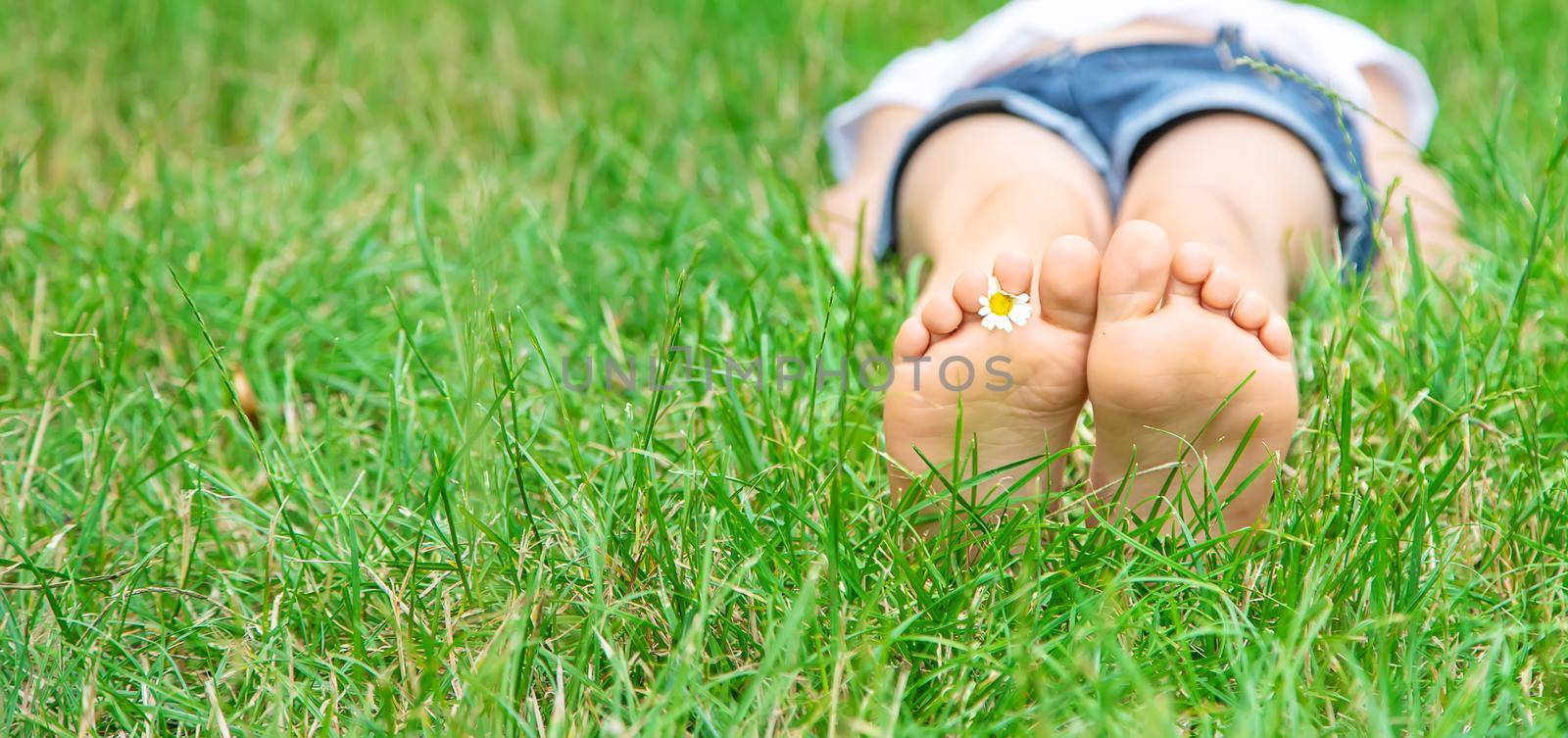 Children's feet with chamomile on green grass. Selective focus. by yanadjana
