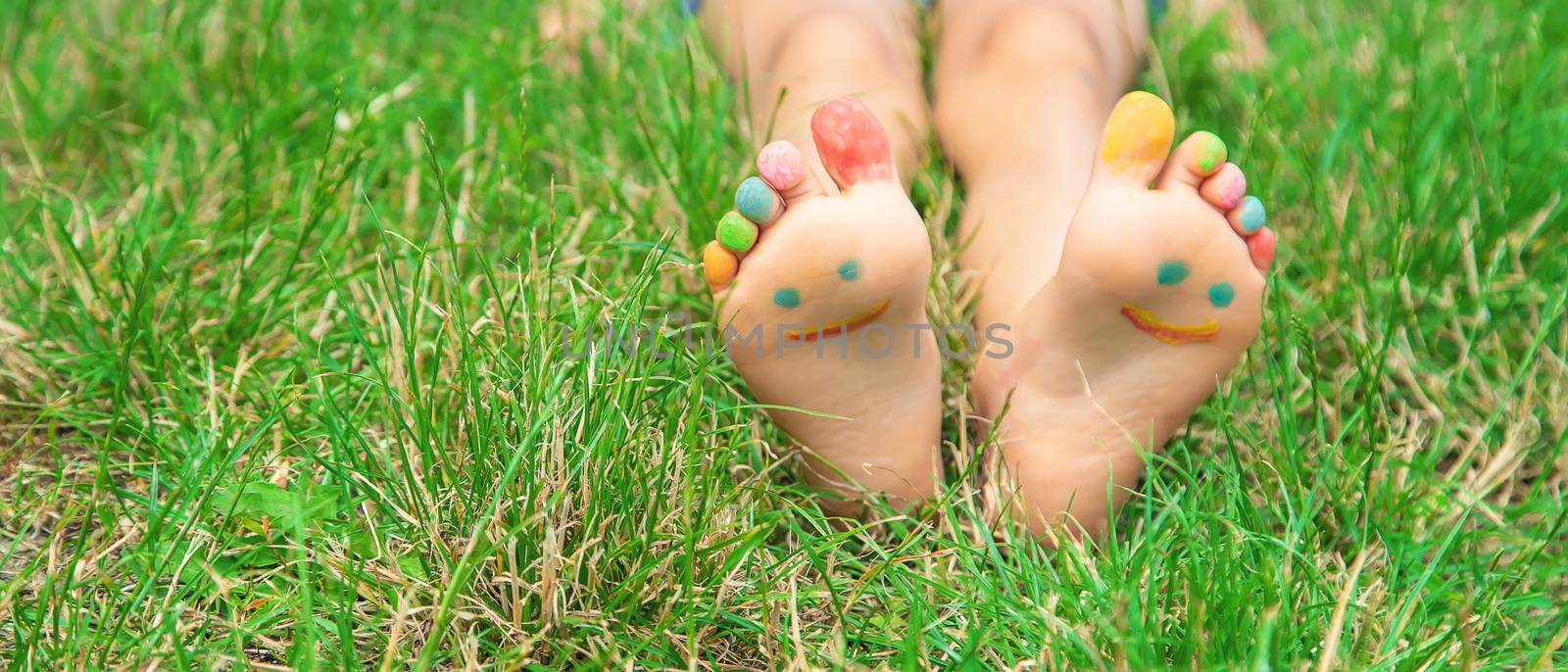 Children's feet with a pattern of paints smile on the green grass. Selective focus. by yanadjana