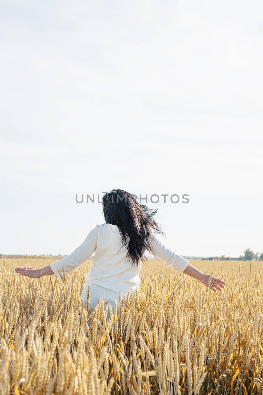 Mid adult woman in white dress standing on a wheat field with sunrise on the background, back view by Desperada