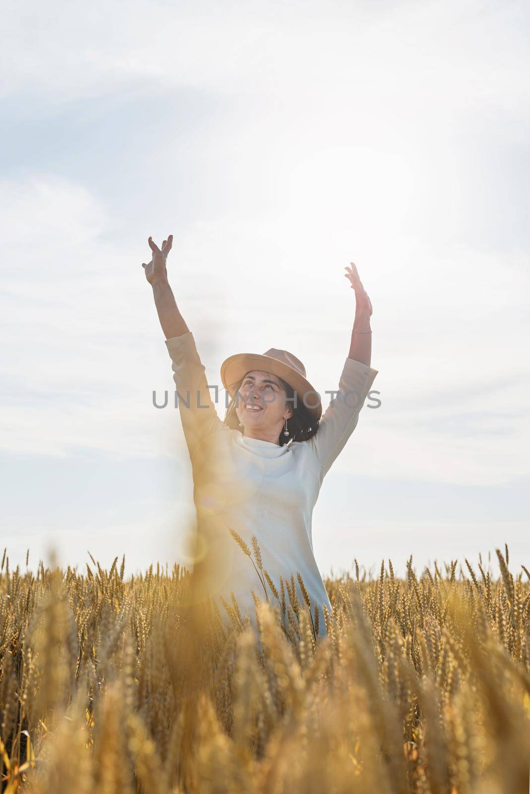 Mid adult woman in white dress standing on a wheat field with sunrise on the background, back view by Desperada