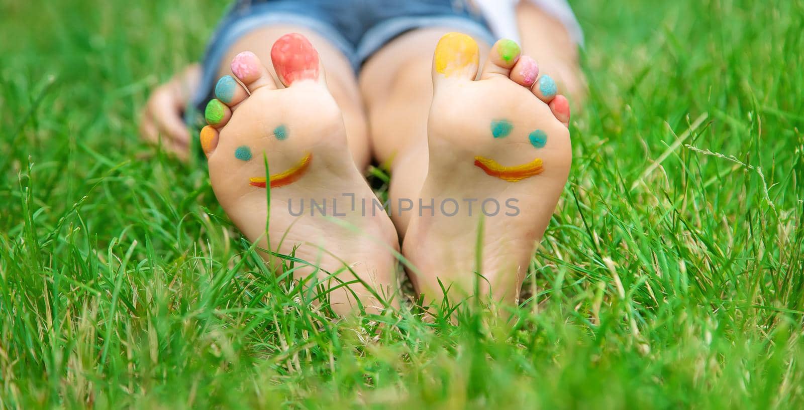 Children's feet with a pattern of paints smile on the green grass. Selective focus. by yanadjana