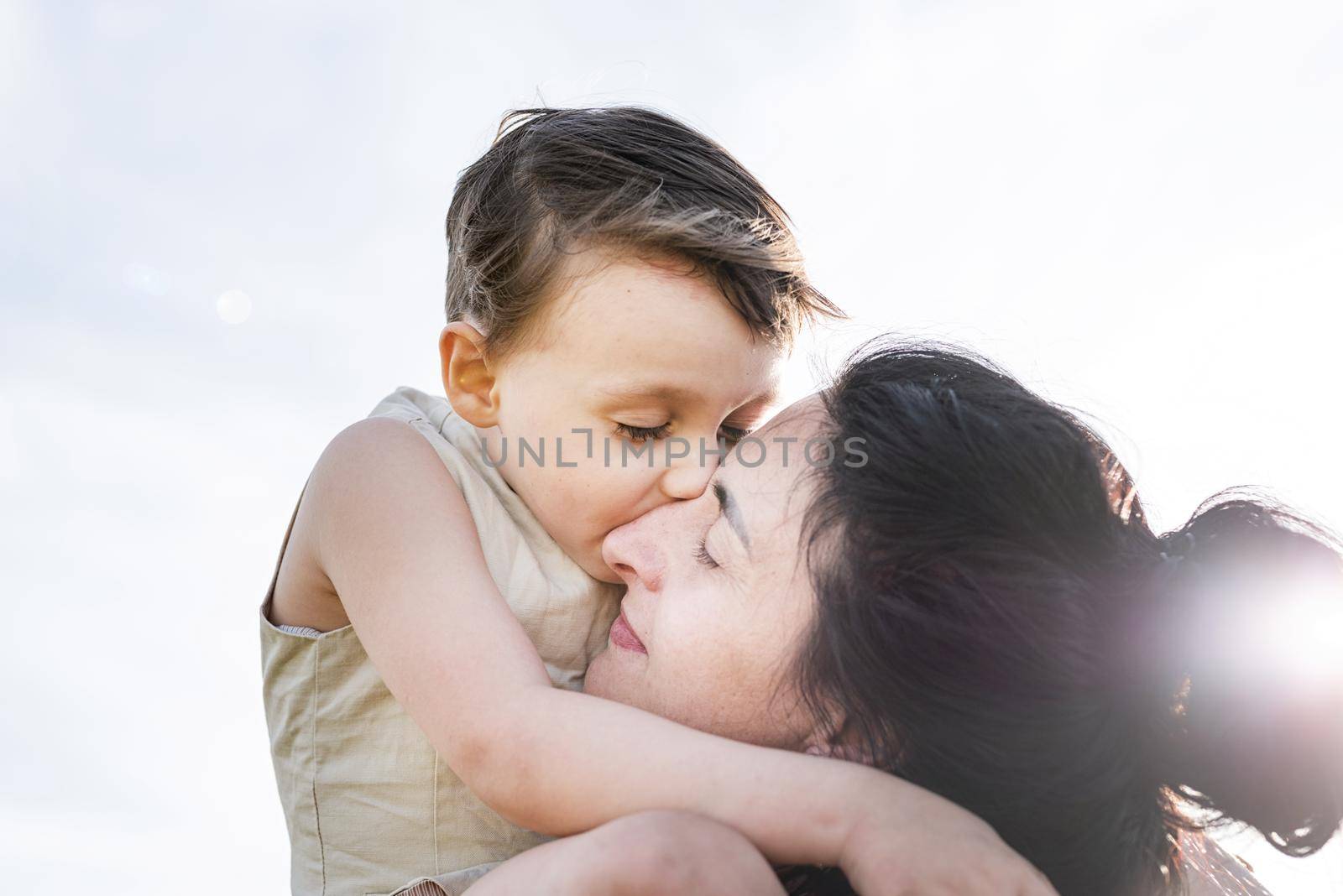 Happy family on a summer walk, mother and child walk in the wheat field and enjoy the beautiful nature, at sunset, hugging and kissing