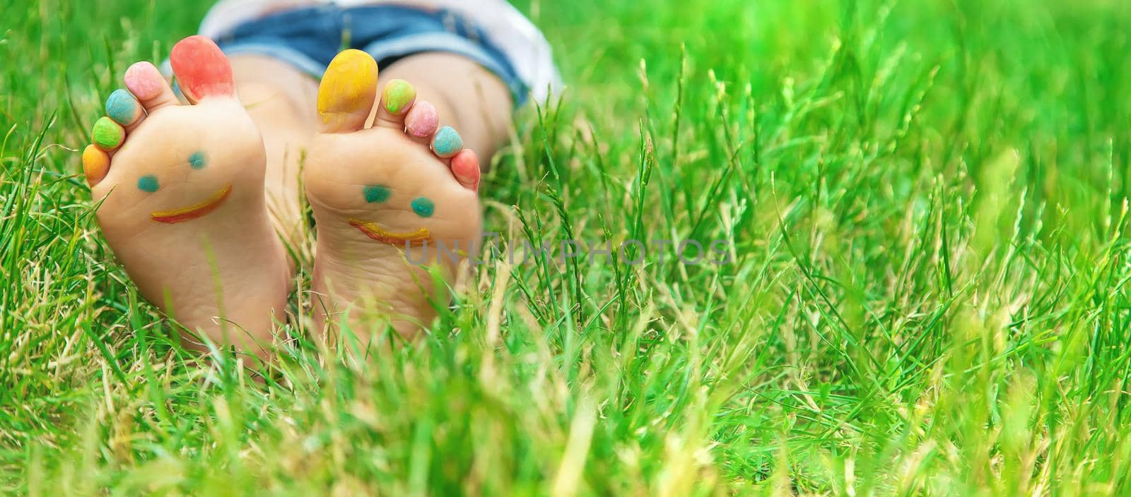 Children's feet with a pattern of paints smile on the green grass. Selective focus. by yanadjana