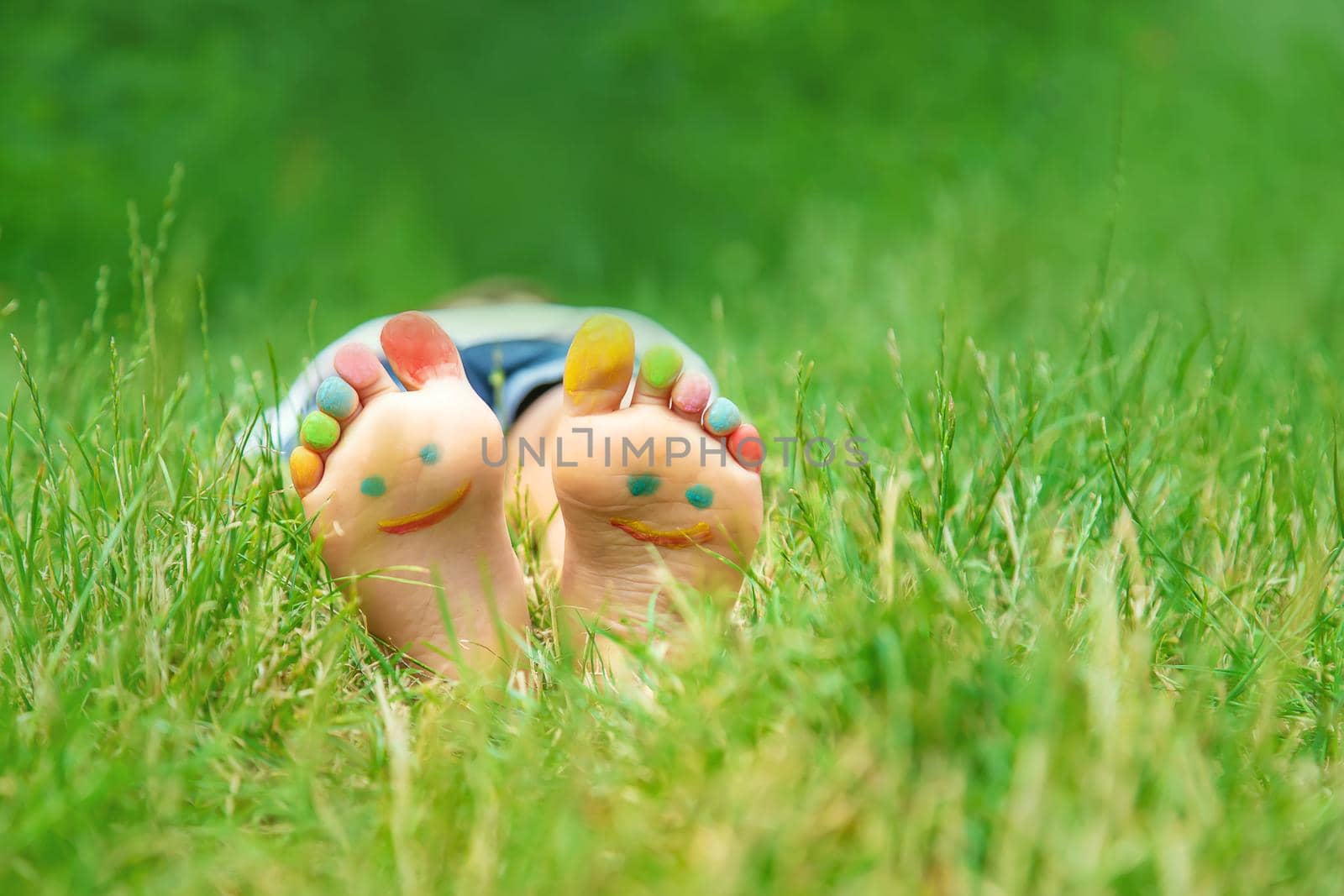 Children's feet with a pattern of paints smile on the green grass. Selective focus. by yanadjana