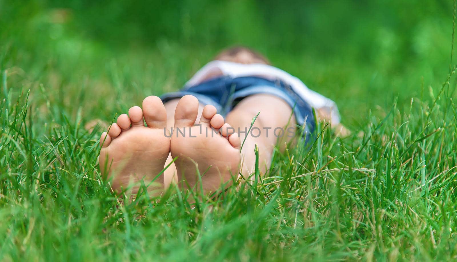 Children's feet on the green grass in the park. Selective focus. by yanadjana