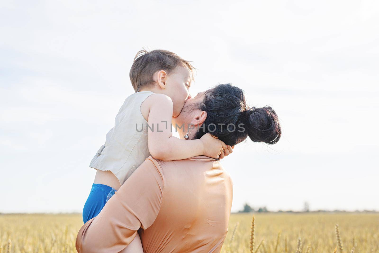 Happy family on a summer walk, mother and child walk in the wheat field and enjoy the beautiful nature, at sunset, hugging and kissing